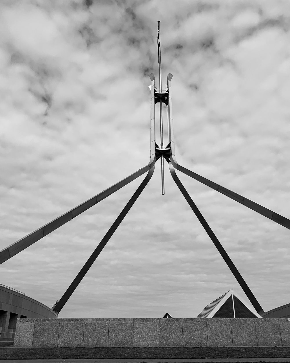 Parliament House, Canberra, its flagpole against a broken sky