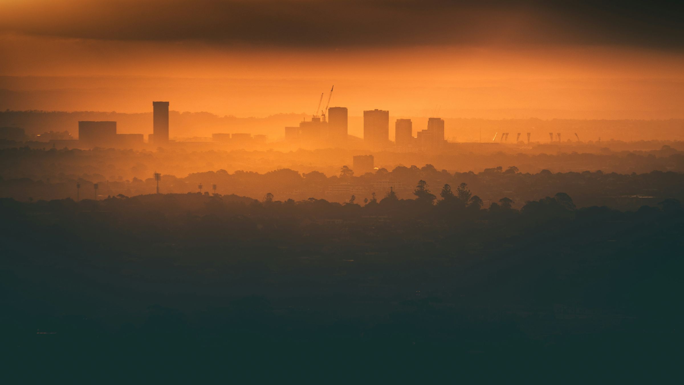 A city skyline in orange haze at sunrise, seen across miles of suburbs