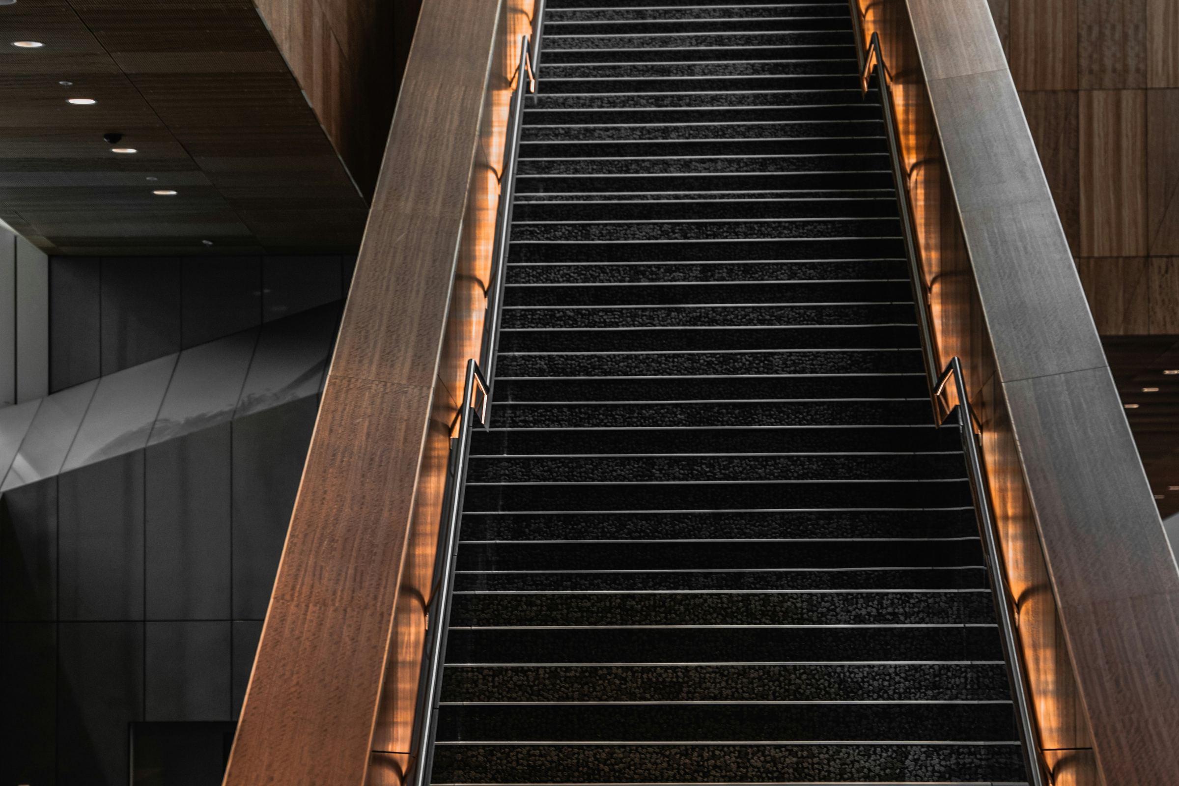 A timber staircase rising through a dark hall, lit from the handrails